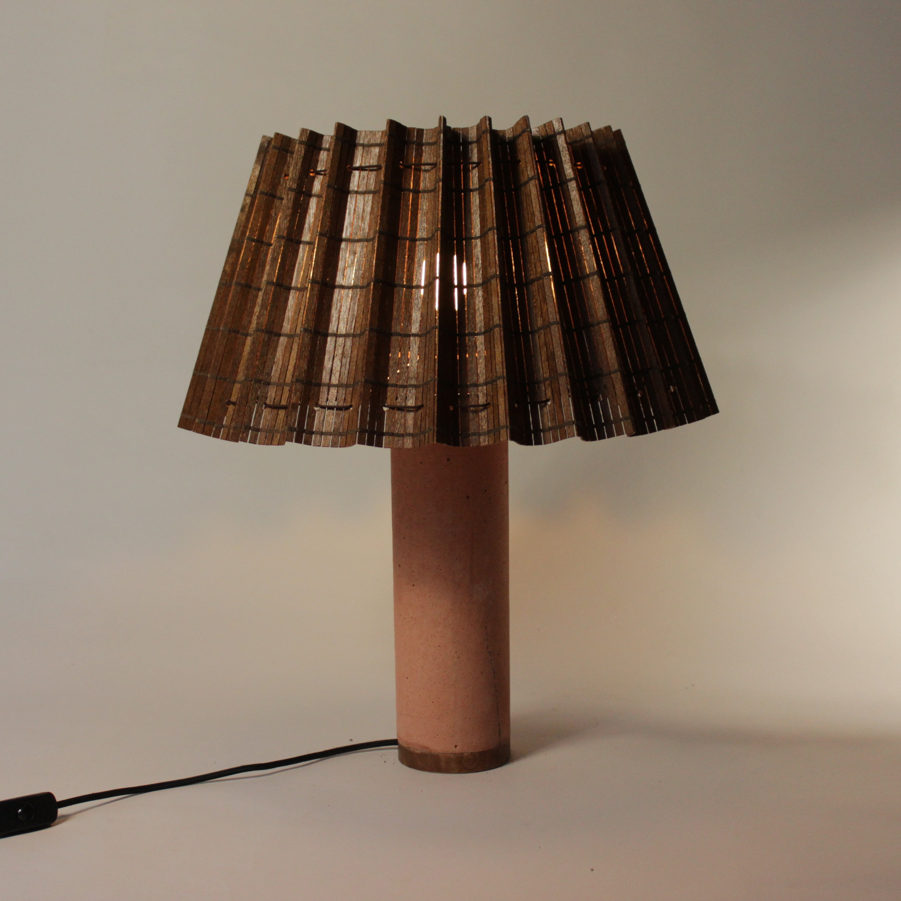 Blikvanger tafellamp met gevouwen kap en warme betonnen voet in terracottakleur. Natuurlijk glans, sculpturale ziel.