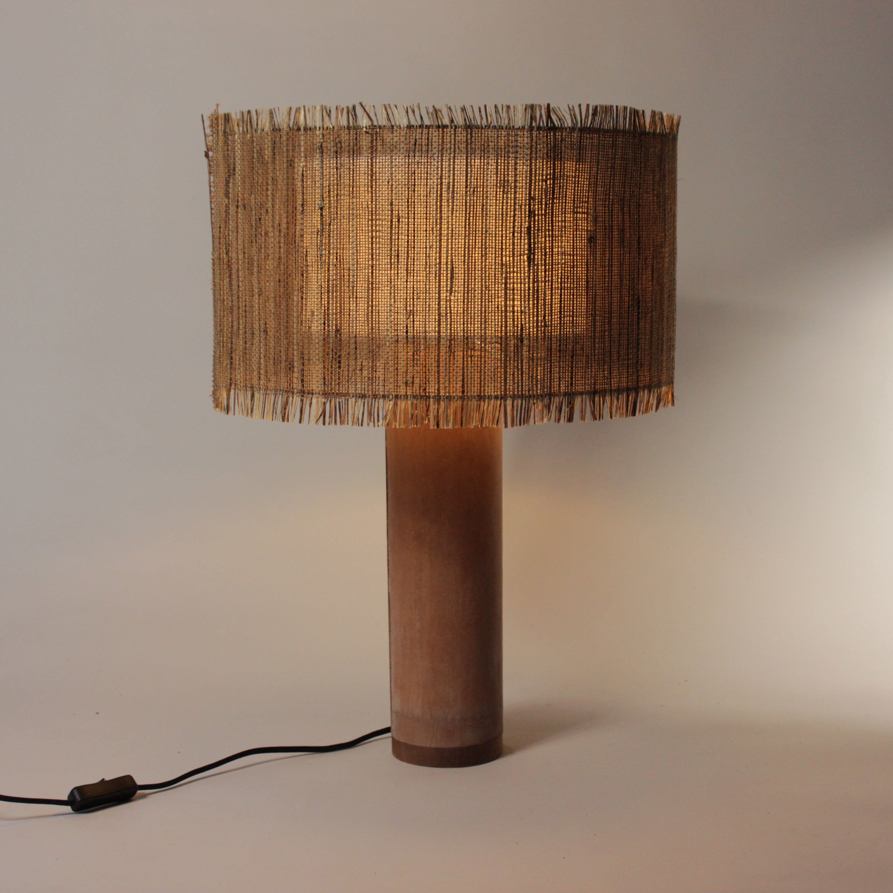 Elegante geweven lamp met terracotta betonvoet, straalt ambachtelijke warmte uit.